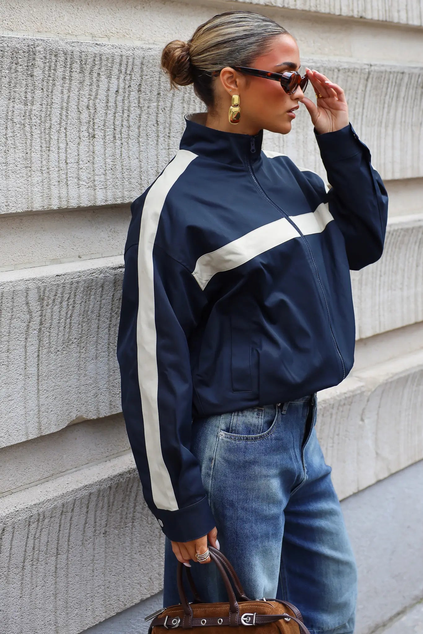 Donkerblauwe track jas dames met hoge kraag beige strepen en ritssluiting gecombineerd met een blauwe wide leg jeans