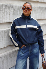 Donkerblauw track jasje met retro sportlook hoge kraag en beige details gecombineerd met een blauwe jeans