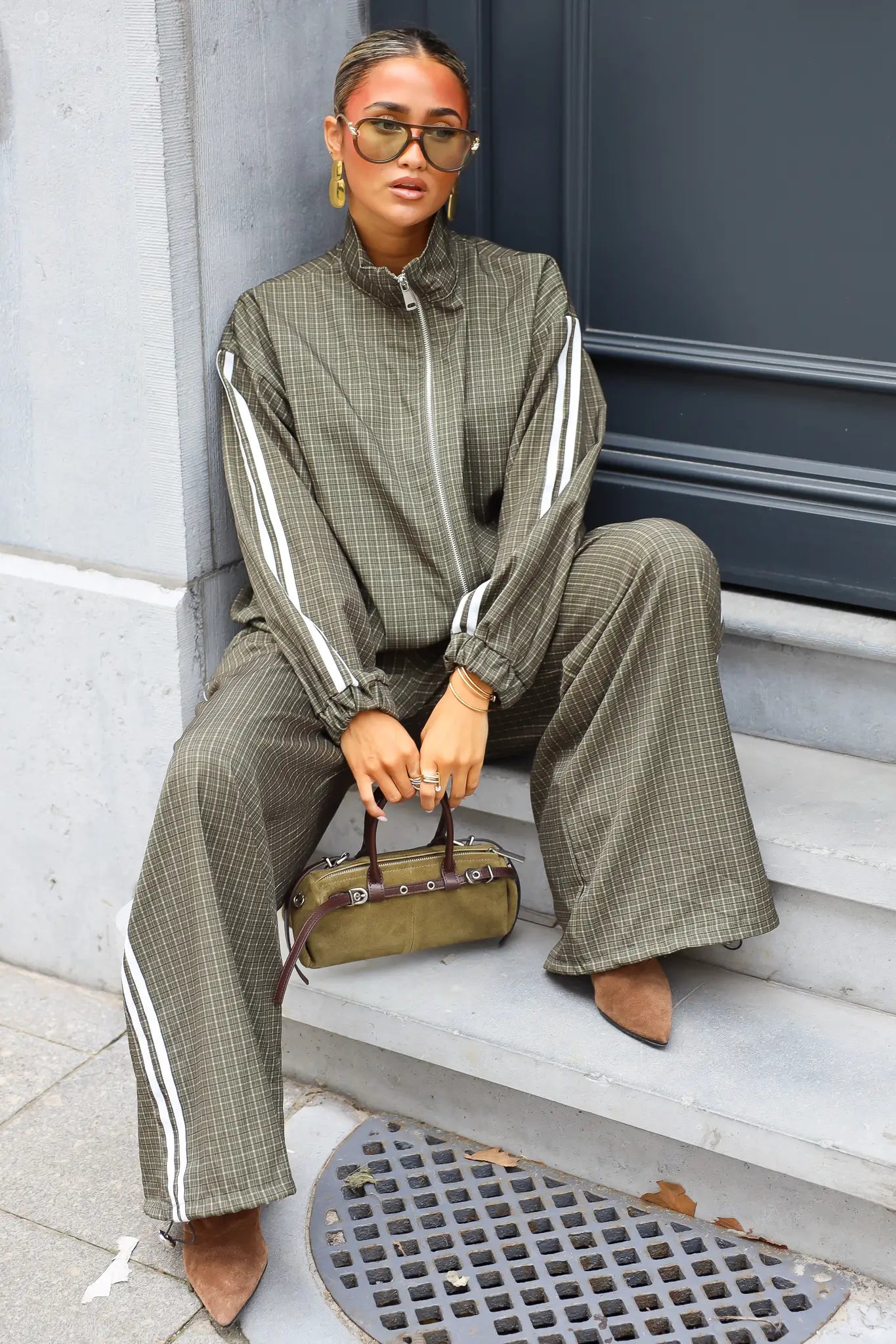 Olijfgroene geruite tracksuit set dames met witte strepen zittend op trap