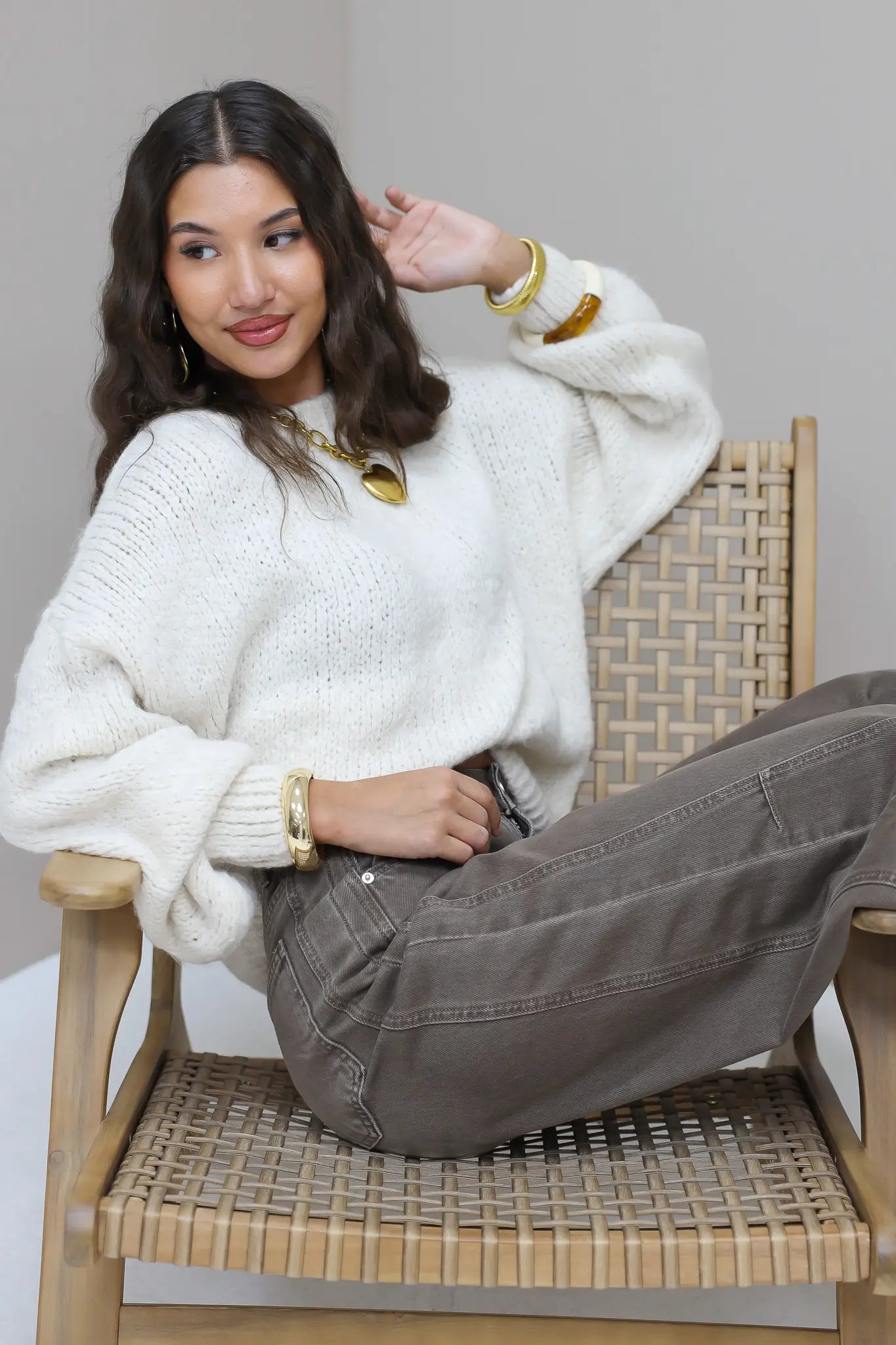 Model in trui wit met bruine broek en opvallende gouden sieraden