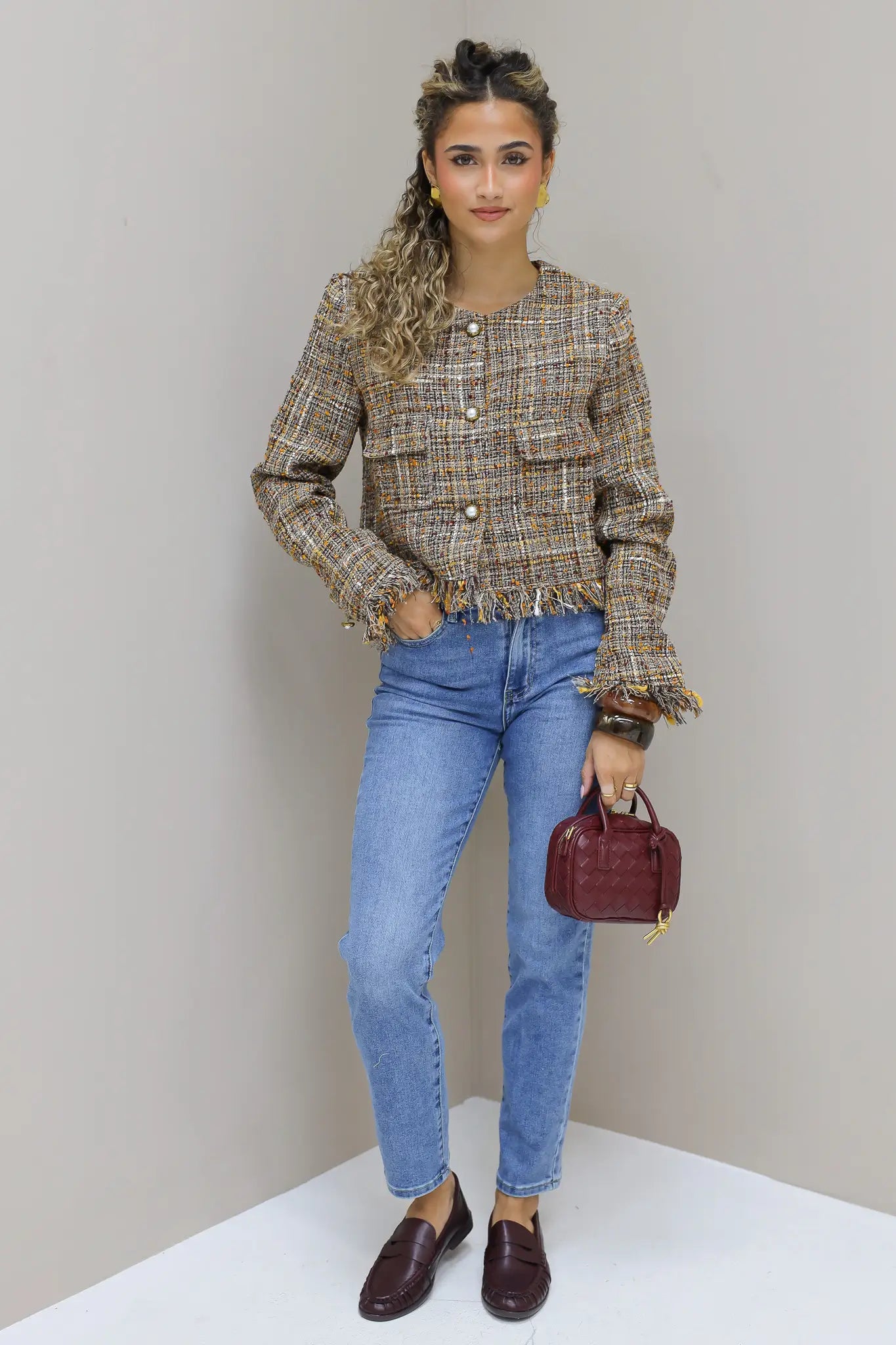 model staat in studio met tweed jasje en jeans en bordeaux tas