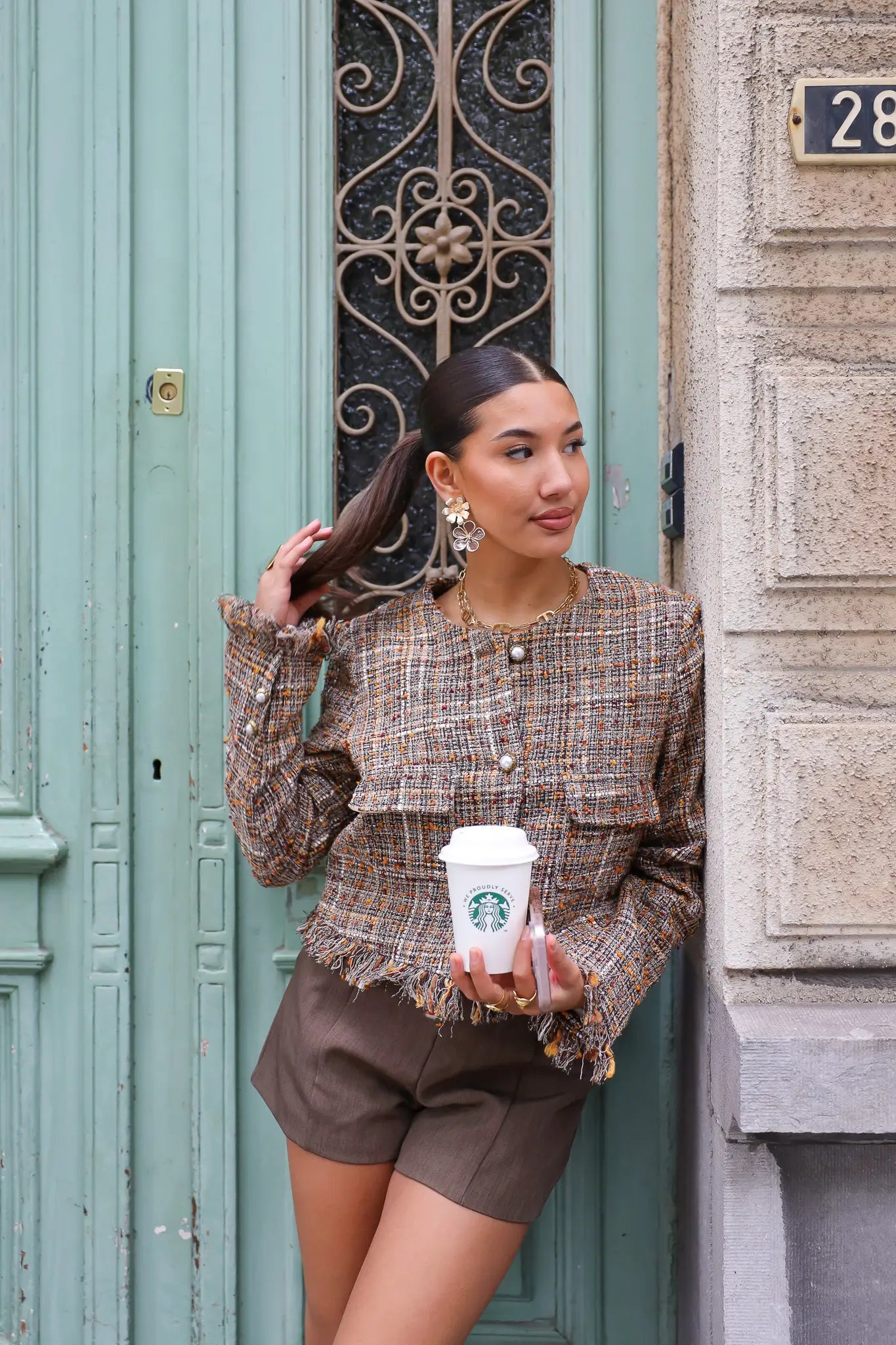 model leunt tegen muur in tweed jasje met koffie in hand