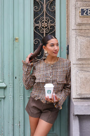model leunt tegen muur in tweed jasje met koffie in hand