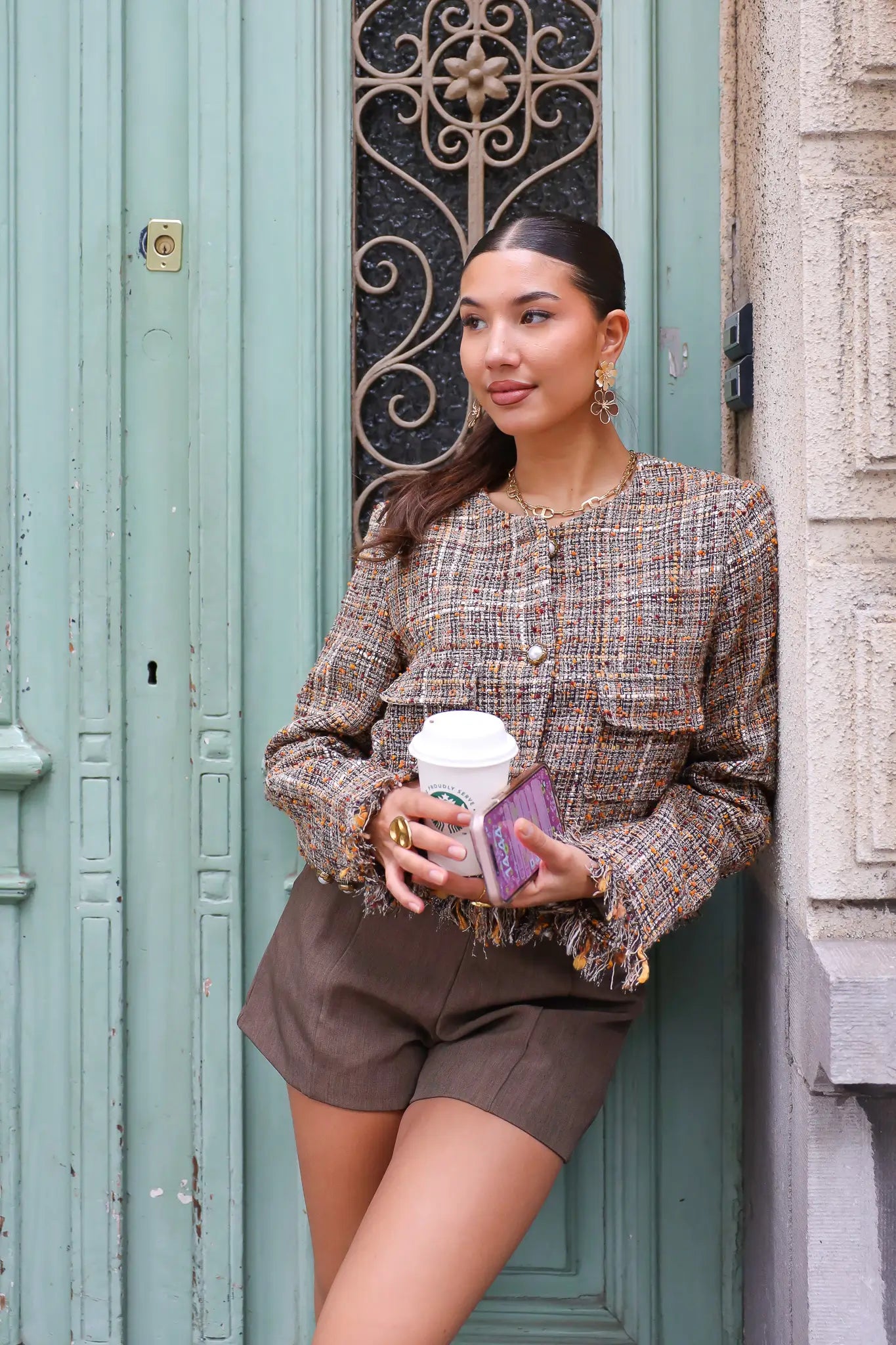 model houdt koffie vast in tweed jasje voor mintgroene deur