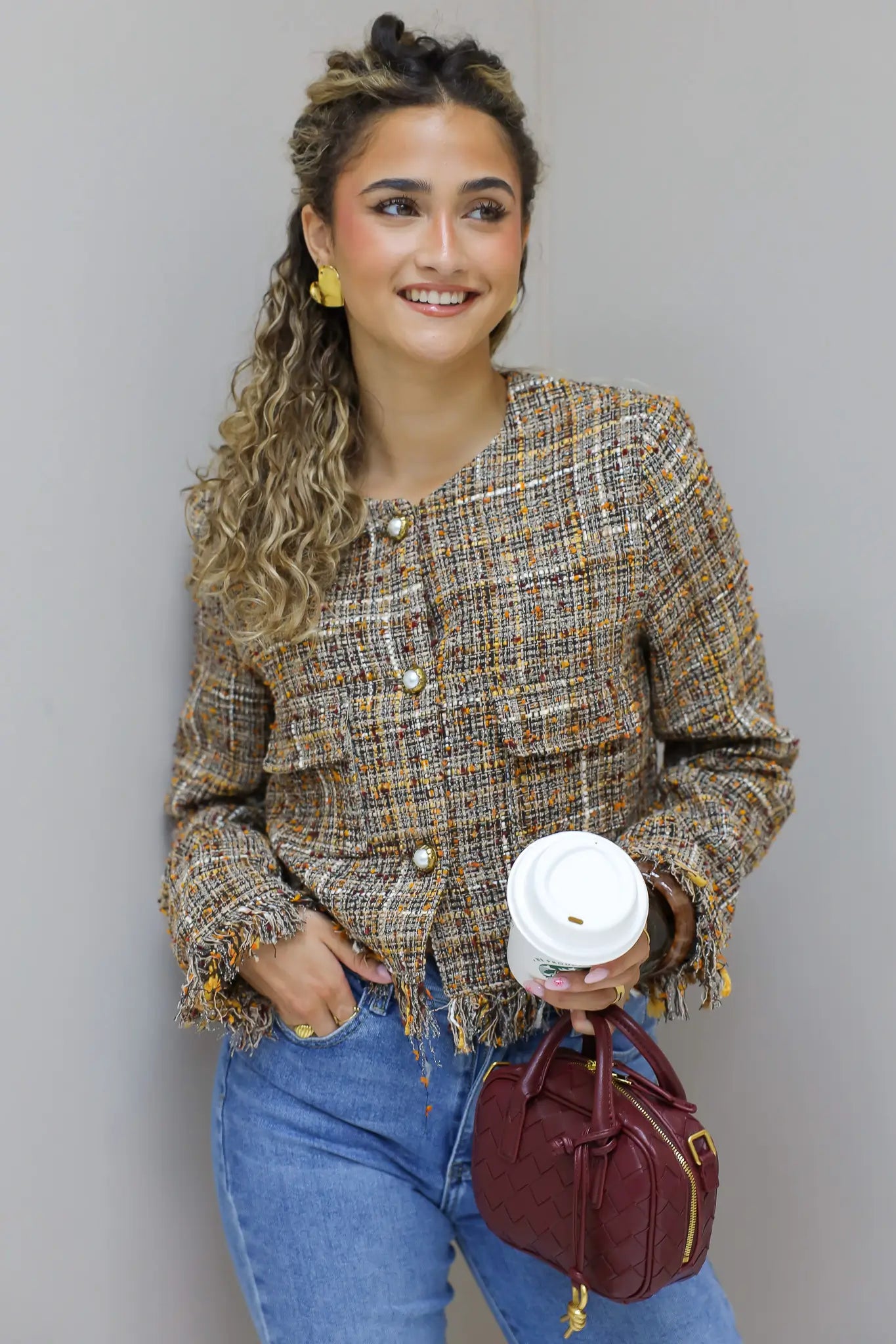 model met tweed jasje houdt koffie vast in studio