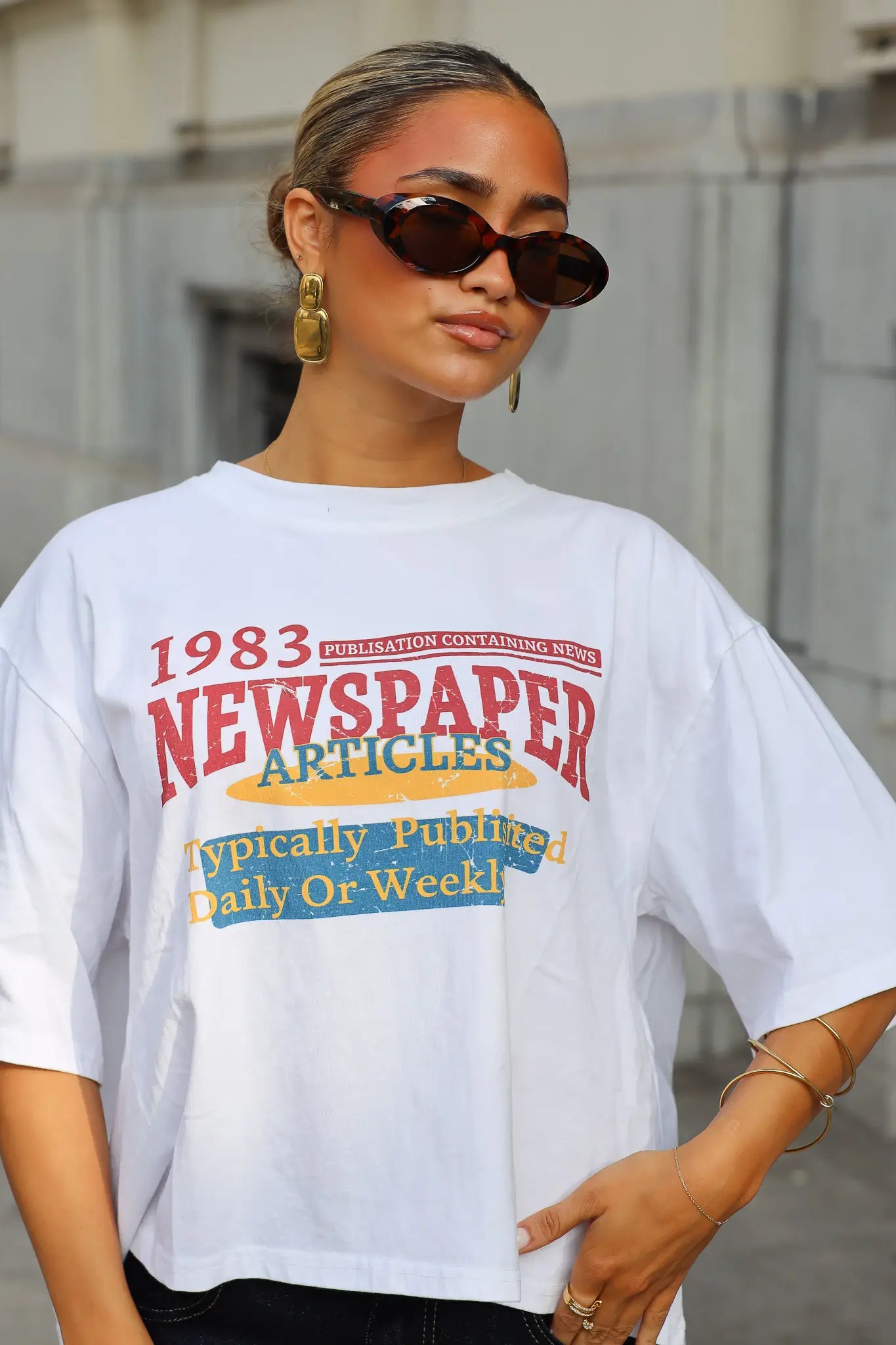 Wit T-shirt met kleurrijke 1983 Newspaper Articles opdruk en ronde hals gecombineerd met een zwarte jeans