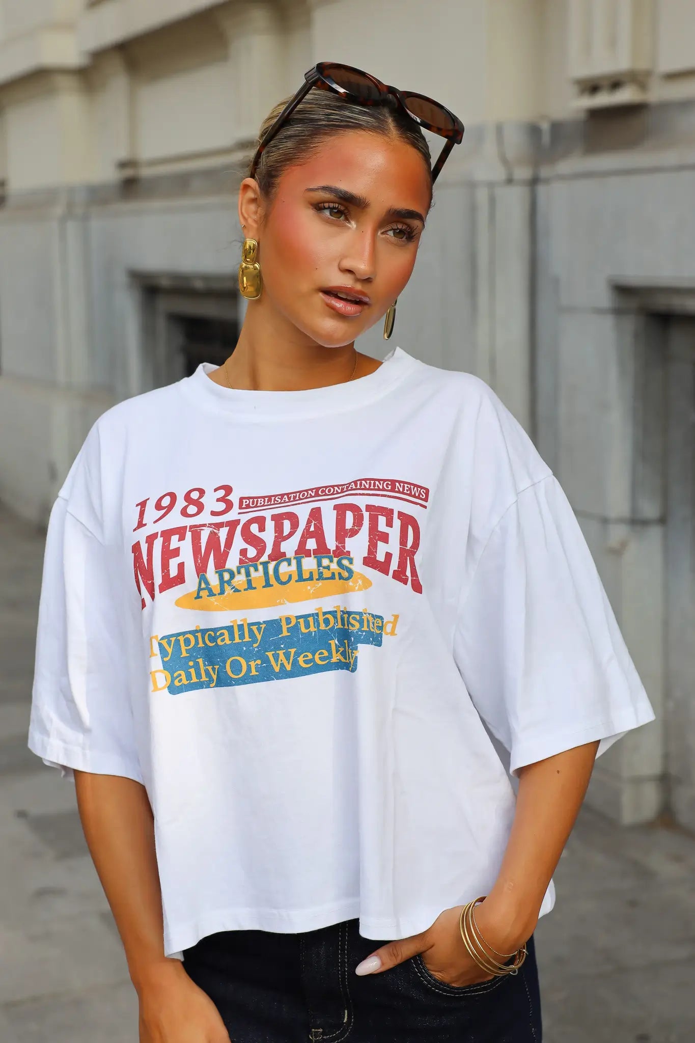Wit T-shirt dames met korte mouwen en kleurrijke 1983 Newspaper Articles opdruk gecombineerd met een zwarte jeans
