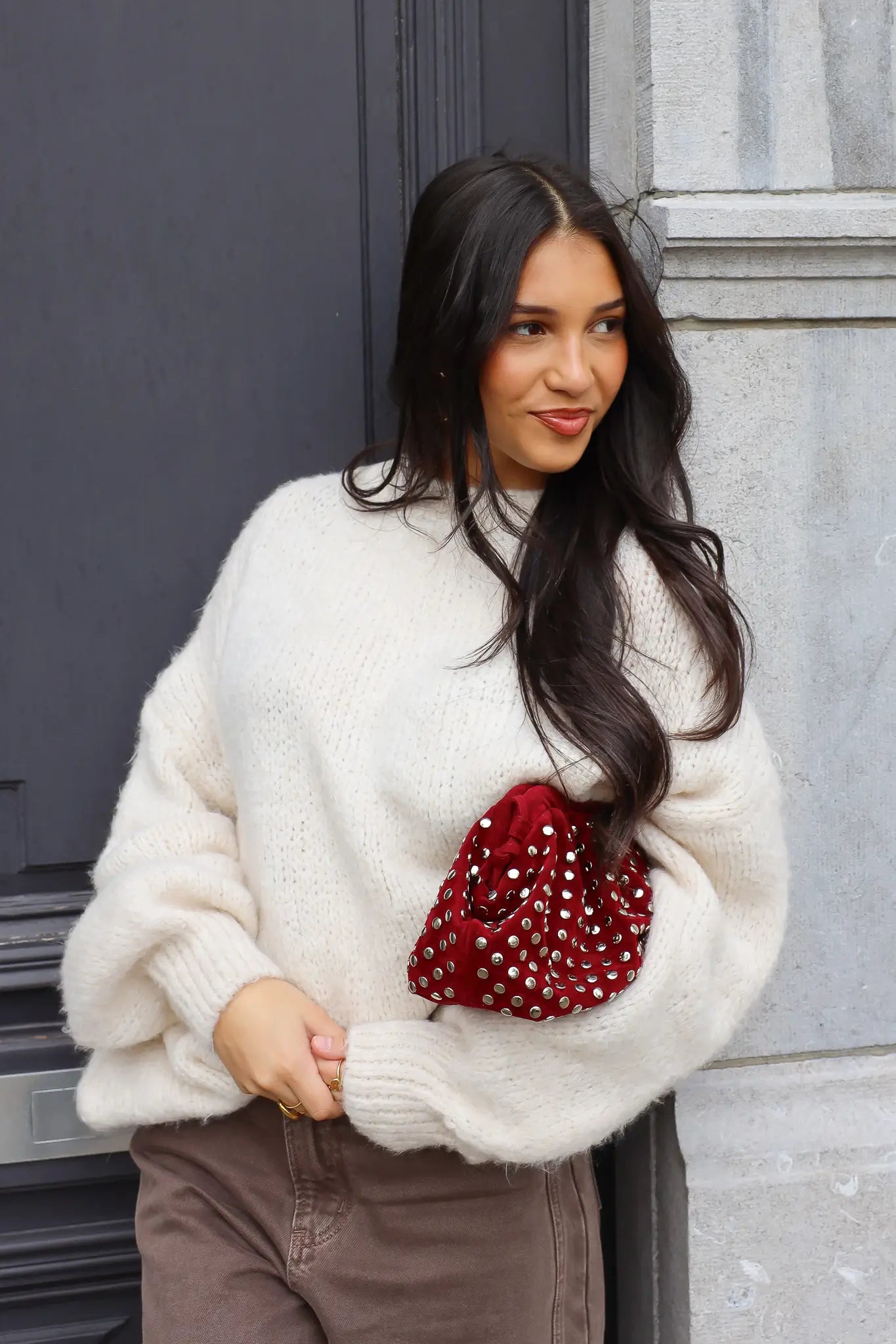 Close-up van witte fluffy trui met bruine broek en rode tas bij deur