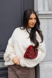 Close-up van witte fluffy trui met bruine broek en rode tas bij deur