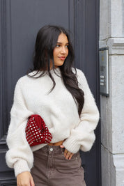 Model draagt witte fluffy trui met bruine broek en rode tas buiten bij zwarte deur