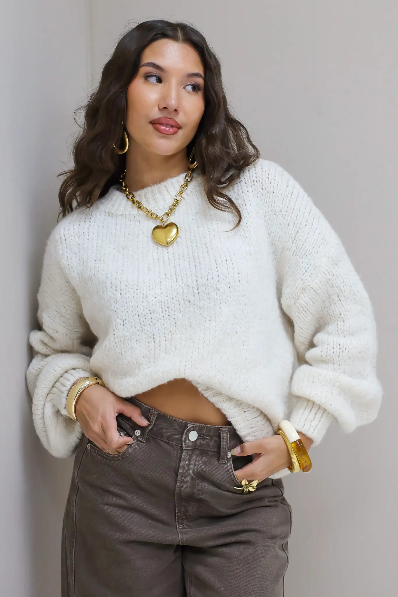 Model draagt witte fluffy trui met bruine broek en gouden sieraden