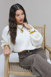 Model zit op houten stoel in witte fluffy trui met bruine broek