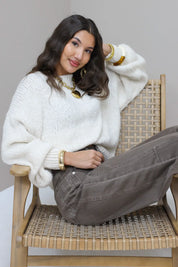 Model poseert op stoel met witte fluffy trui en bruine broek