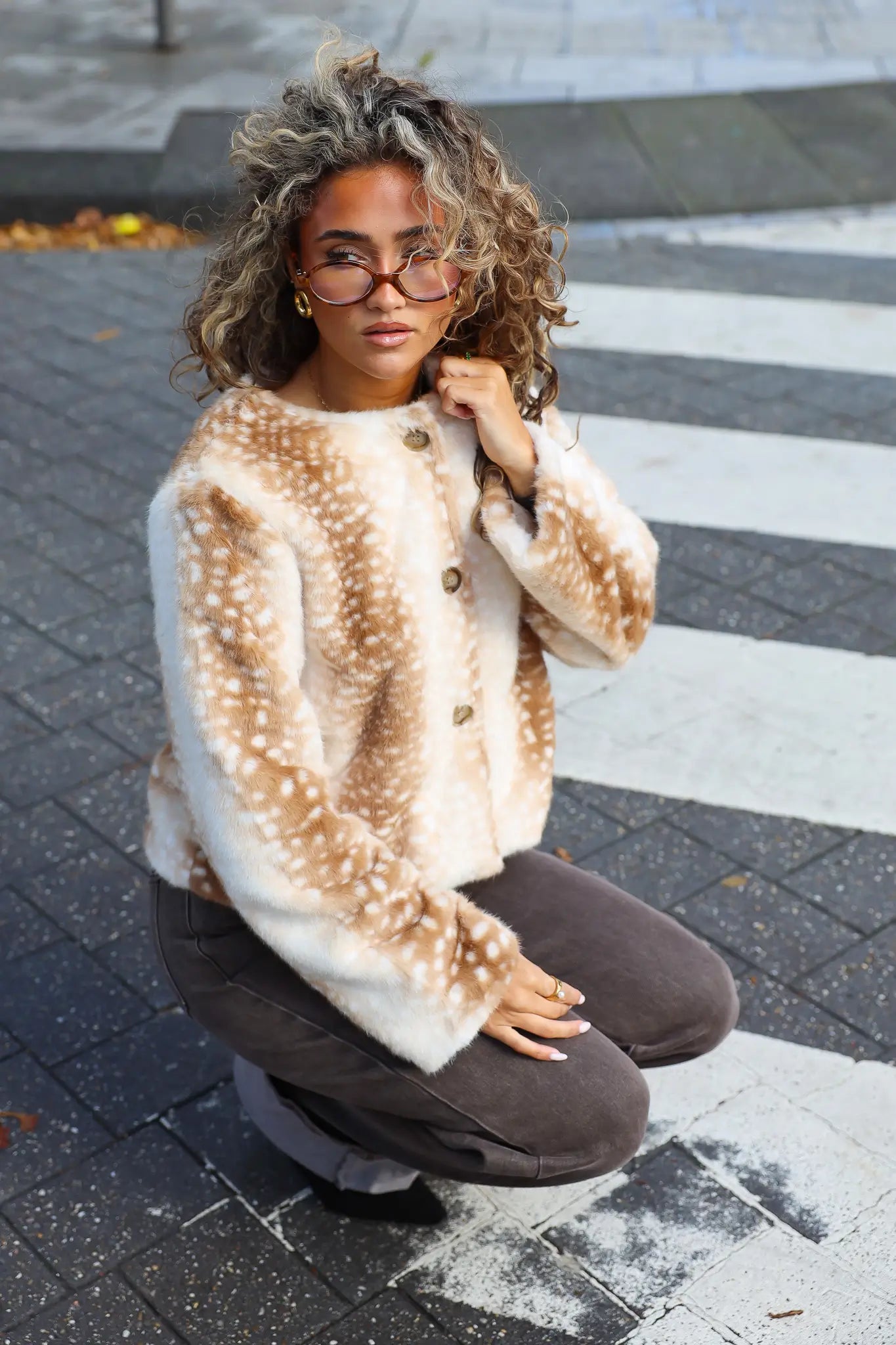 Zachte Bambi jas camel met beige en bruine hertenprint gecombineerd met een donkerbruine jeans terwijl het model op straat zit