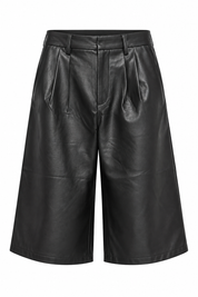 Detail van zwarte faux leather bermuda met plooien aan de voorkant en brede broekspijpen