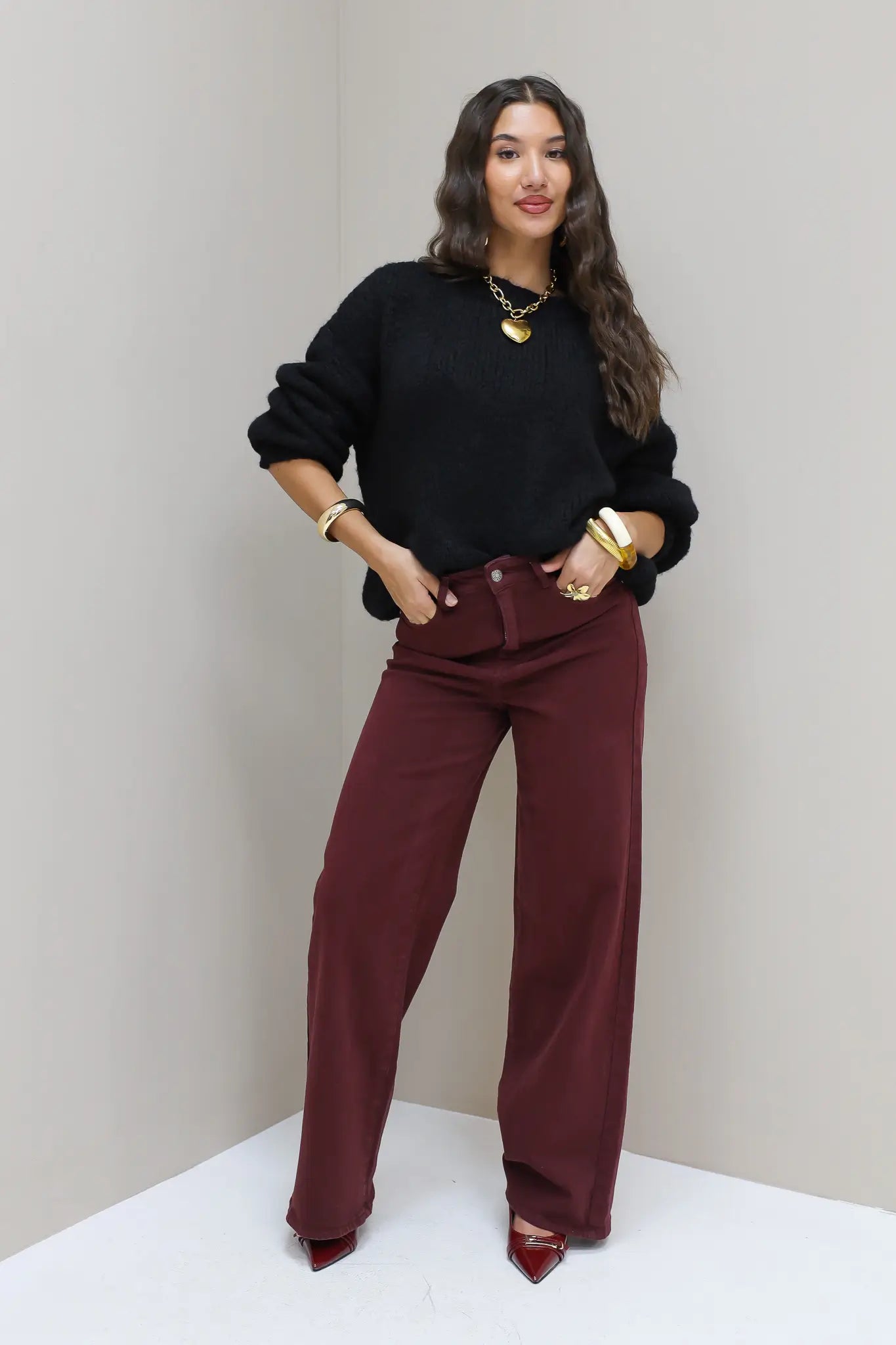Model staat frontaal in zwarte cropped trui met bordeaux broek en hakken