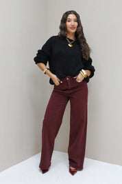 Model staat frontaal in zwarte cropped trui met bordeaux broek en hakken