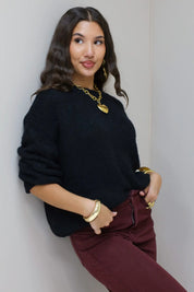 Model lacht in zwarte cropped trui met bordeaux broek en gouden sieraden