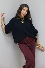 Model staat recht in zwarte cropped trui met bordeaux broek