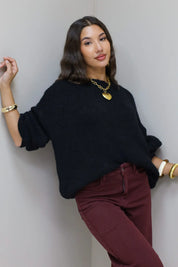 Model draagt zwarte cropped trui met bruine broek en poseert buiten