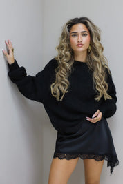 Model met zwarte cropped trui en kort rokje tegen lichte muur