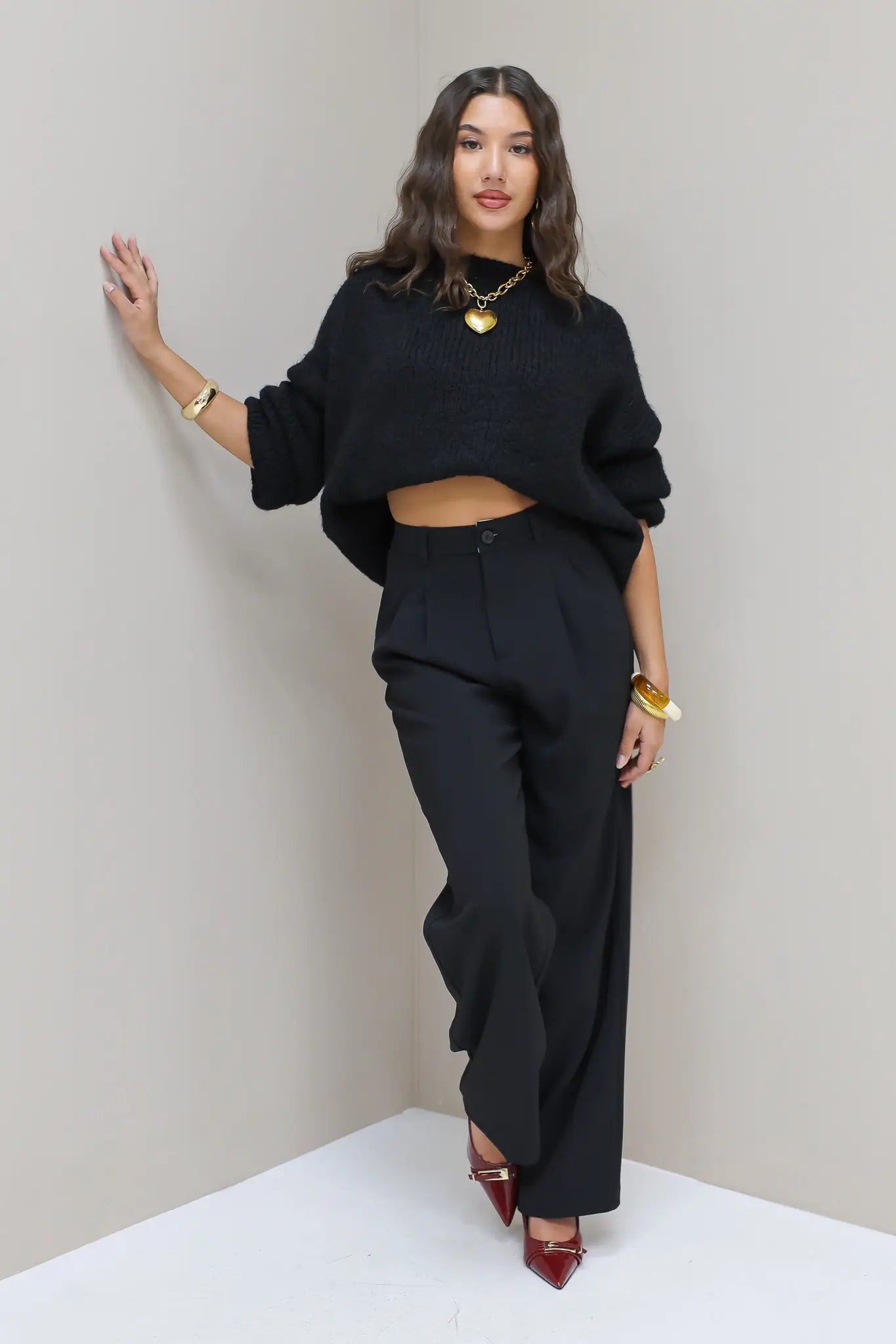 Model leunt tegen muur met zwarte pantalon en zwarte trui