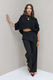 Model leunt tegen muur met zwarte pantalon en zwarte trui