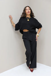 Model leunt tegen muur in zwarte pantalon en zwarte trui