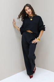 Model poseert in hoek met zwarte pantalon en zwarte trui