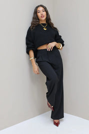 Model kijkt schuin met zwarte pantalon en zwarte trui