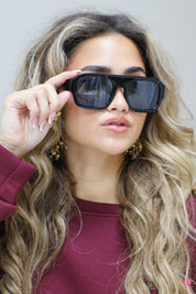 model met zwarte zonnebril en golvend haar raakt de bril aan en kijkt richting camera