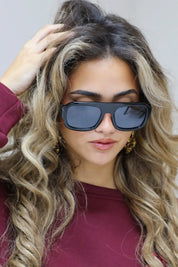 model met zwarte zonnebril houdt haar vast en kijkt licht omhoog