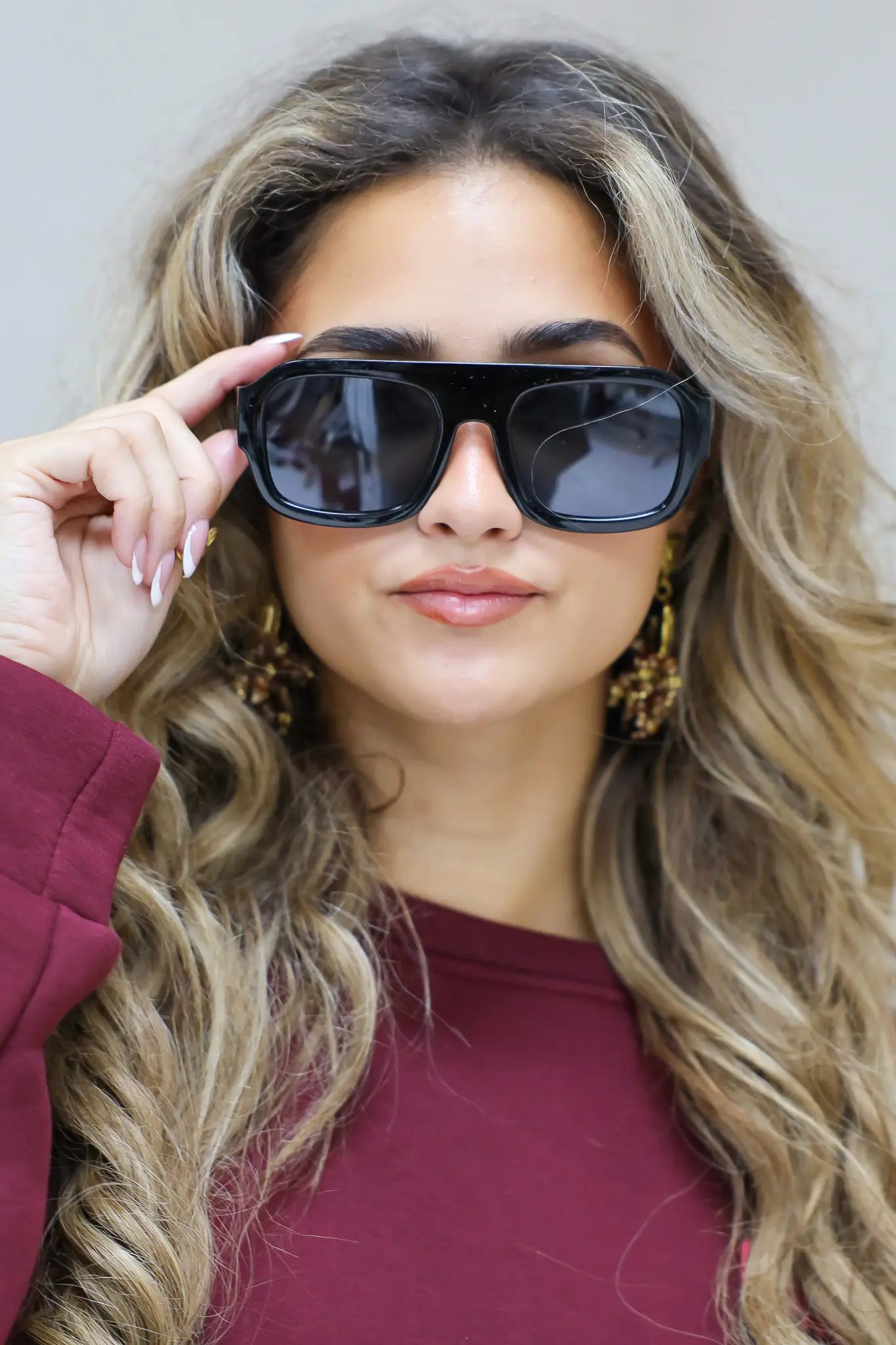 model met zwarte zonnebril kijkt recht in de camera met hand bij de bril