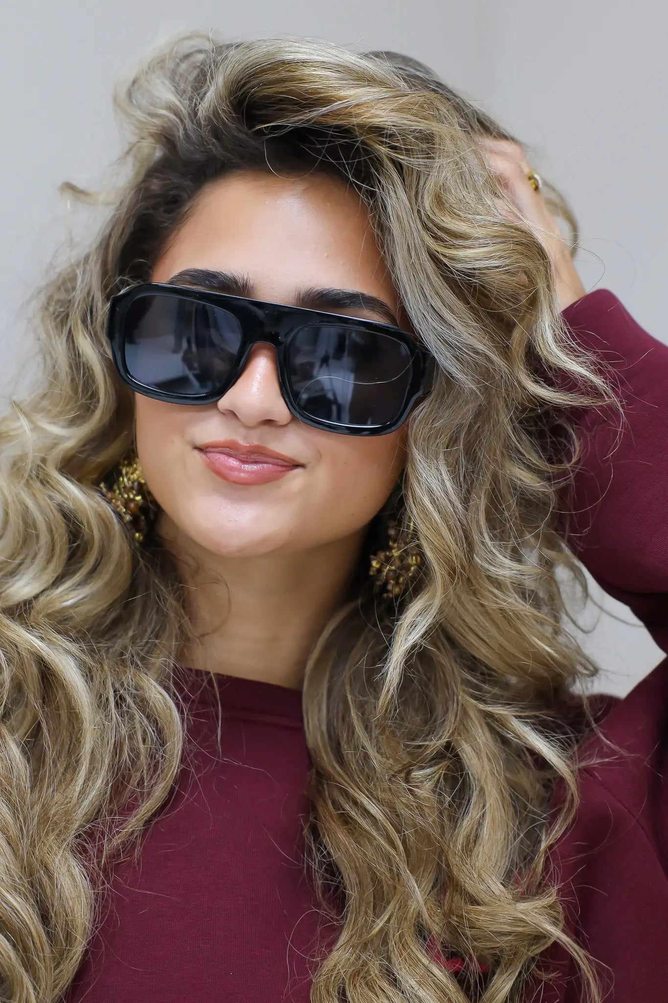 model met zwarte zonnebril kijkt recht vooruit en draagt een bordeaux top