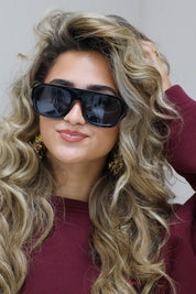 model met zwarte zonnebril kijkt recht vooruit en draagt een bordeaux top